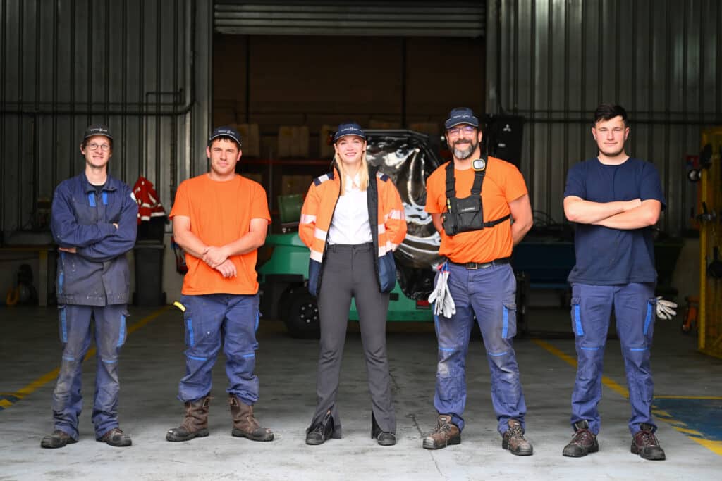 A diverse production team poses together inside the malt facility, representing collaboration across departments.