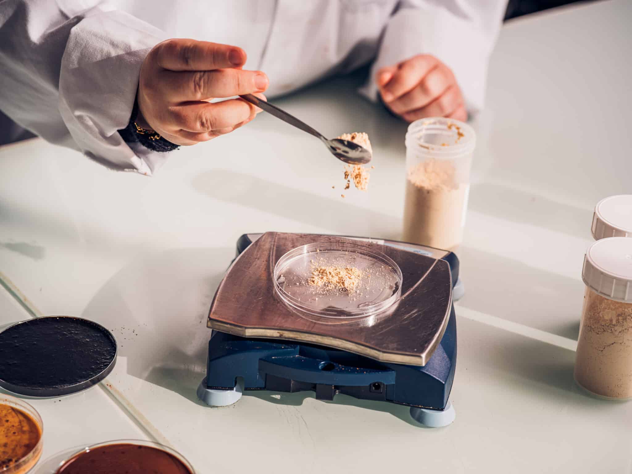 A food scientist precisely measures malt powder in a laboratory, supporting malt innovation through product development and quality testing.