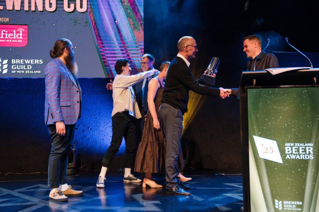 An award recipient accepts recognition on stage during [Event Name], celebrating excellence in brewing.